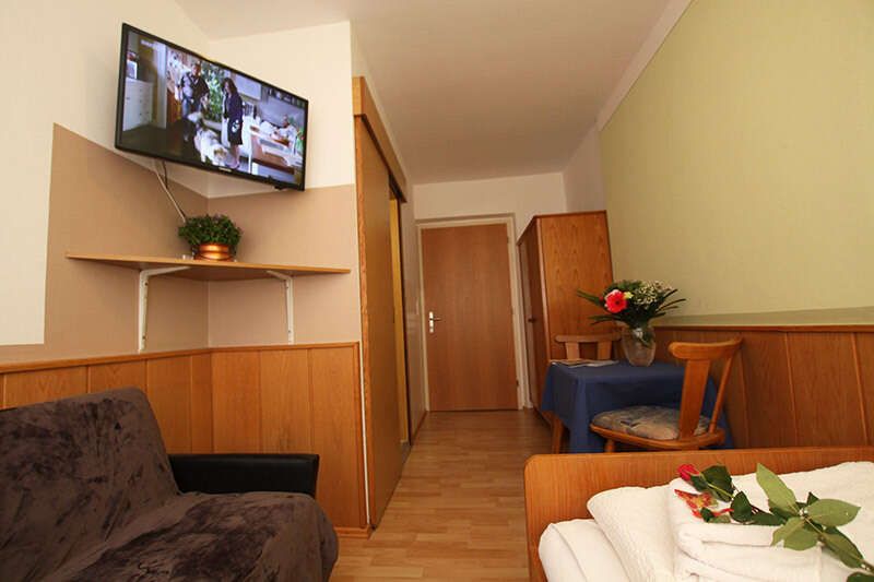 Einzelzimmer mit TV, Tisch mit Stühlen und Couch 